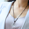 A person wearing a clear round stone pendant on a black cord against a white top