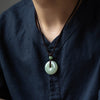 Person wearing a pale green jade peace buckle pendant on a dark cord against a blue shirt
