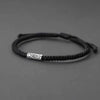 Close up of a black woven bracelet with a silver koi fish charm on a gray background