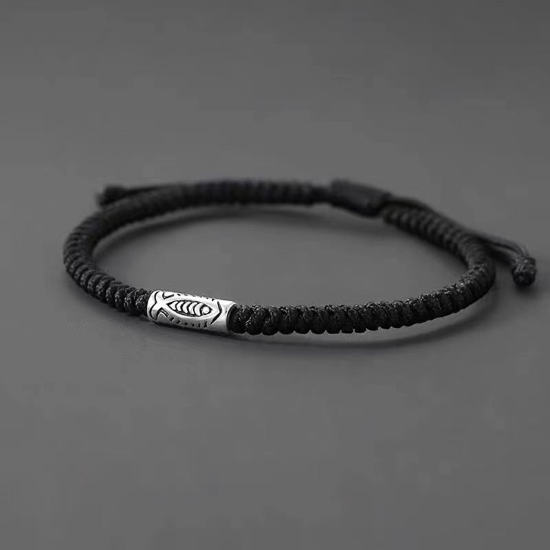 Close up of a black woven bracelet with a silver koi fish charm on a gray background