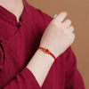 Close up of a red woven cord bracelet with a gold peace buckle and red agate bead on a wrist