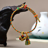 Close up of a multi-colored woven rope bracelet with a golden ball and zongzi charm