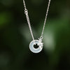 Close up of a silver necklace with a white round stone pendant and flower charm