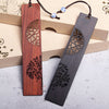 Two wooden bookmarks with tree designs, one reddish brown and one dark grey, resting on a beige box