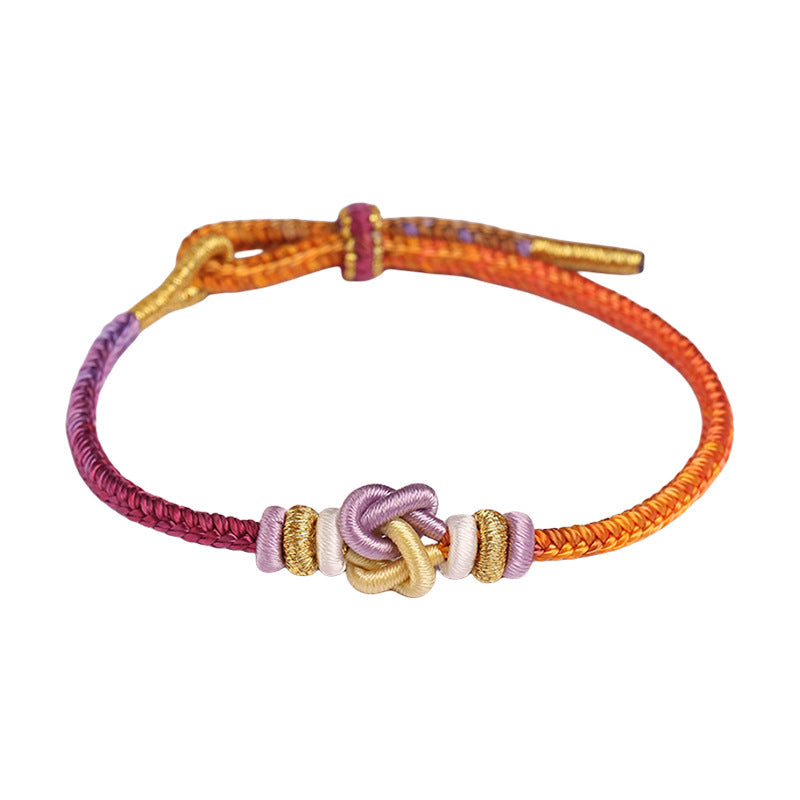 Close-up of a multicolor braided cord bracelet with a central heart knot on a red background