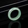 A polished light green natural stone ring sitting on a dark surface