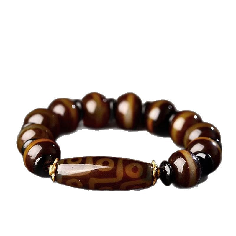 Hand holding a brown agate bracelet with a long central Dzi bead