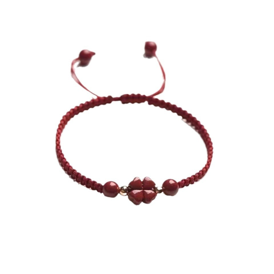 Close up of a red woven bracelet with a cinnabar flower charm and gold beads
