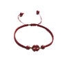 Close up of a red woven bracelet with a cinnabar flower charm and gold beads