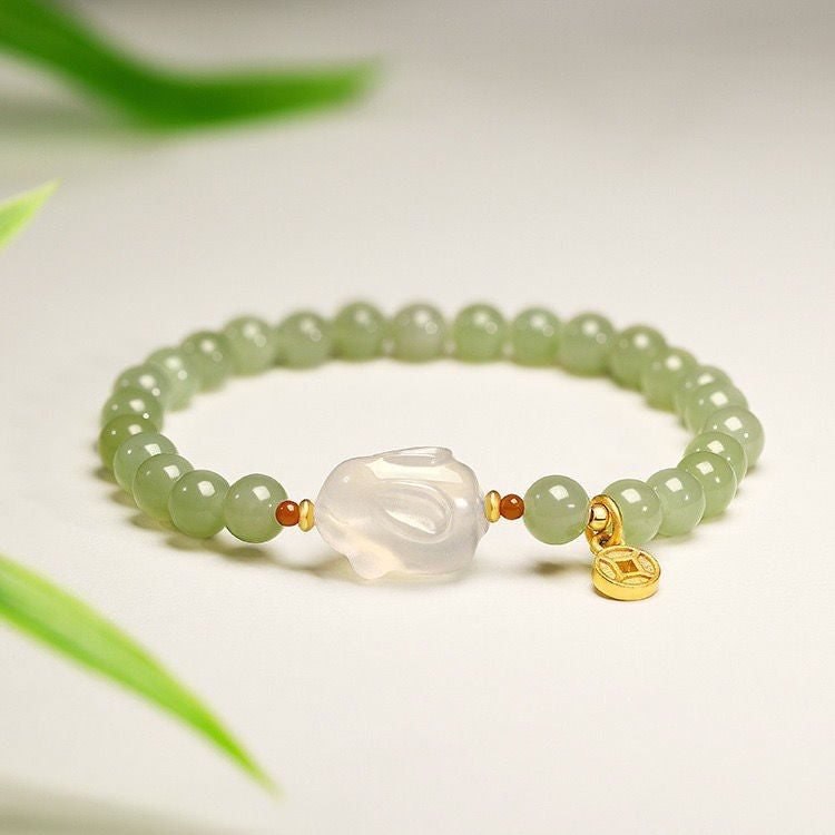 Light green beaded bracelet with a central white rabbit carving and a small gold coin charm
