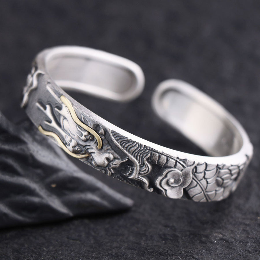 Close up of a silver open cuff bracelet with a carved dragon design and gold highlights