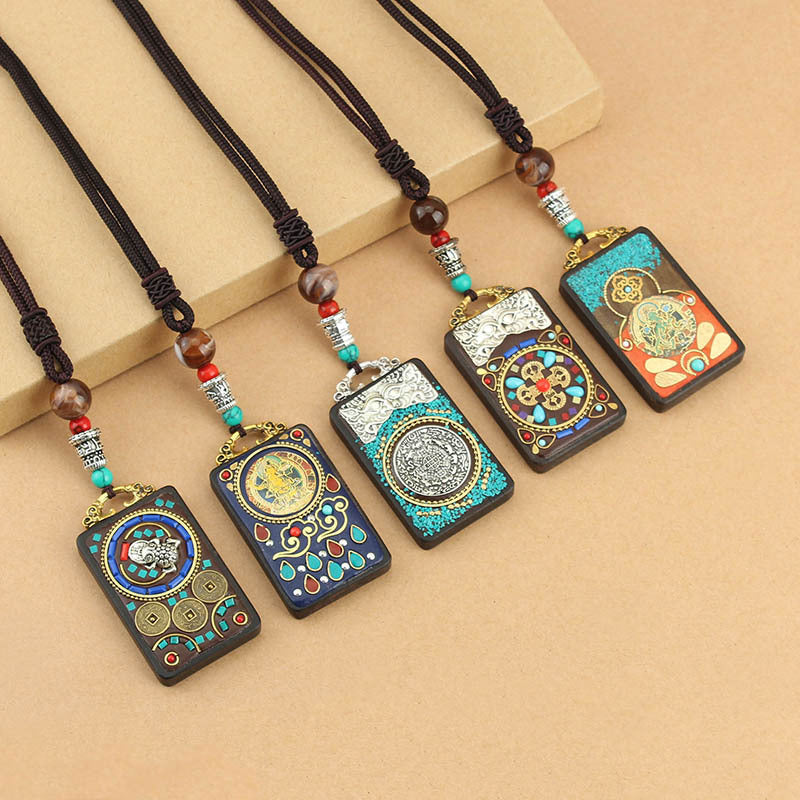 Five Tibetan thangka pendant necklaces with colorful designs on dark wood displayed on a beige background.