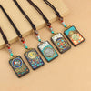 Five Tibetan thangka pendant necklaces with colorful designs on dark wood displayed on a beige background.