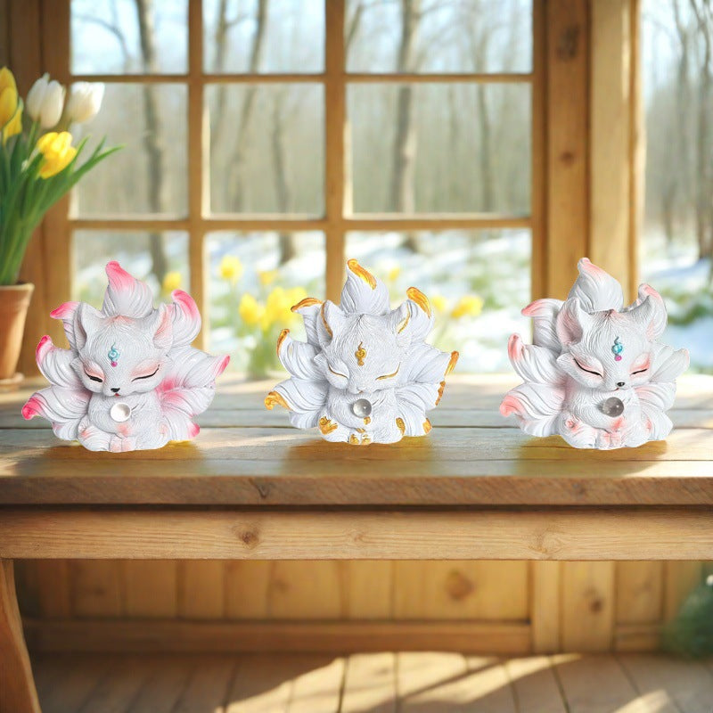 Three small resin nine-tailed fox statues sitting on a wooden bench near a window