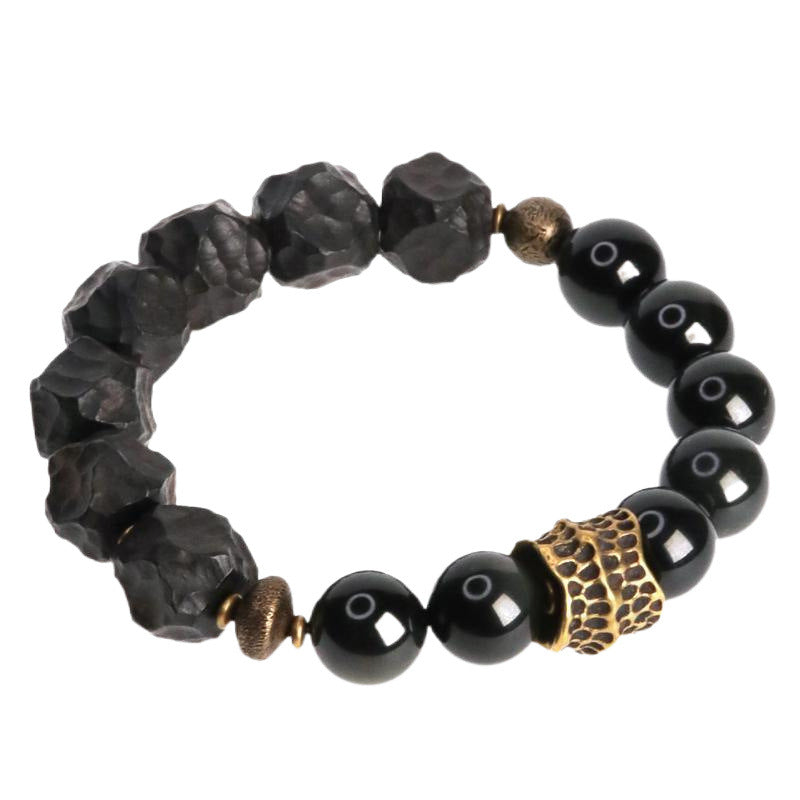 Close-up of a black obsidian bracelet with textured stones and a gold-tone honeycomb bead