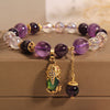 Close-up of an amethyst and clear quartz beaded bracelet with a gold Pixiu charm on a box.
