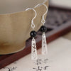 A pair of silver tone drop earrings with black beads and floral cutouts