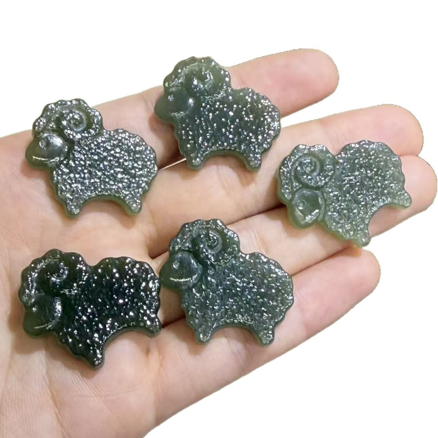 Five dark green carved jade sheep pendants resting on an open palm