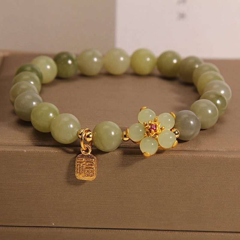 Green jade bead bracelet with gold four leaf clover and Fu charm on a box