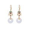 Gold tone drop earrings with white circular pendants on a wooden surface