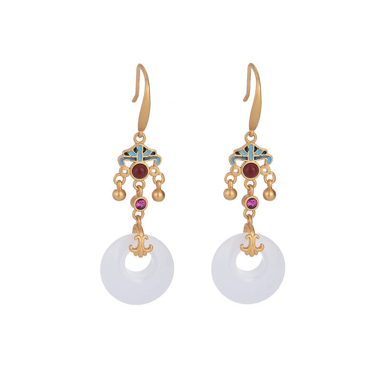Gold tone drop earrings with white circular pendants on a wooden surface