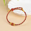 Close-up of a red and green woven bracelet with gold-tone ends on a beige surface