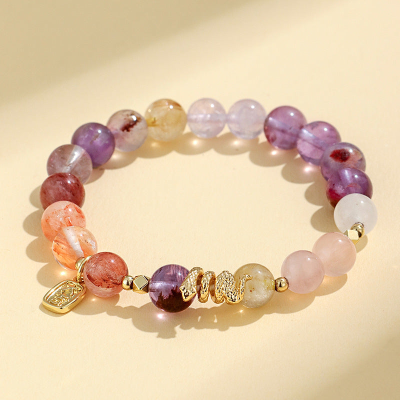 Close-up of a multi-colored crystal beaded bracelet with a gold snake charm on a cream background.