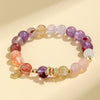 Close-up of a multi-colored crystal beaded bracelet with a gold snake charm on a cream background.