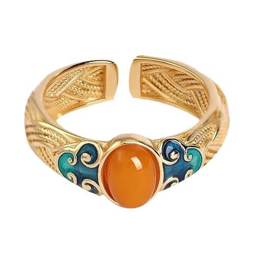 Gold-tone copper ring with blue enamel clouds and orange stone on a fabric background