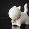 Close-up of a white ceramic cat tea pet with a red collar and gold bell