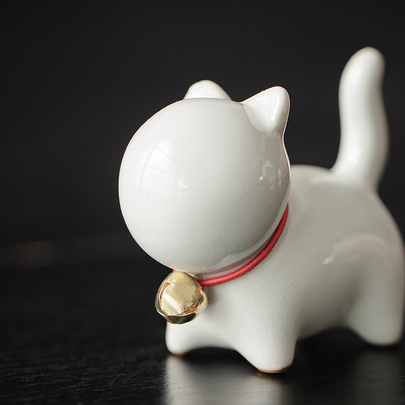Close-up of a white ceramic cat tea pet with a red collar and gold bell