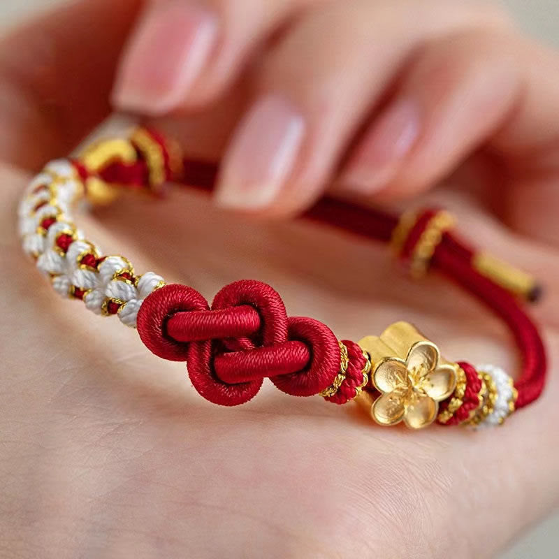 Close up of a red woven bracelet with a gold flower charm on a wrist