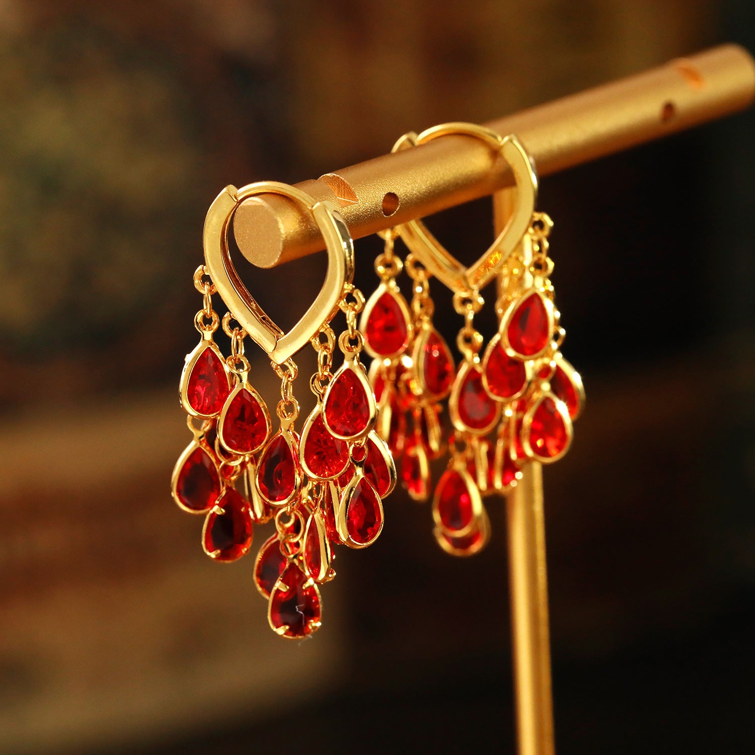 Gold-tone copper hoop earrings with hanging red water droplet charms on a display stand