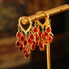 Gold-tone copper hoop earrings with hanging red water droplet charms on a display stand