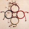Three woven bracelets in black, red, and multi-color with cinnabar charms on a textured background