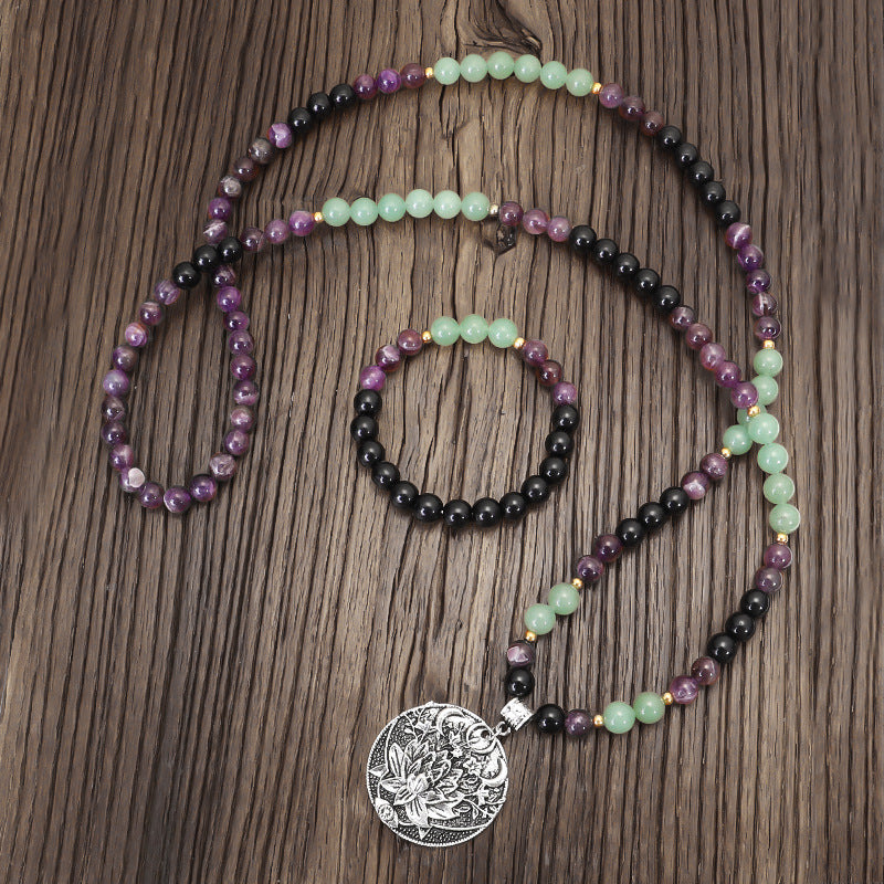 Coiled 108 bead mala necklace with purple and green stones and a large silver lotus pendant on wood