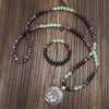 Coiled 108 bead mala necklace with purple and green stones and a large silver lotus pendant on wood