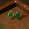 Pair of oval green chalcedony stud earrings with gold rim on wooden surface