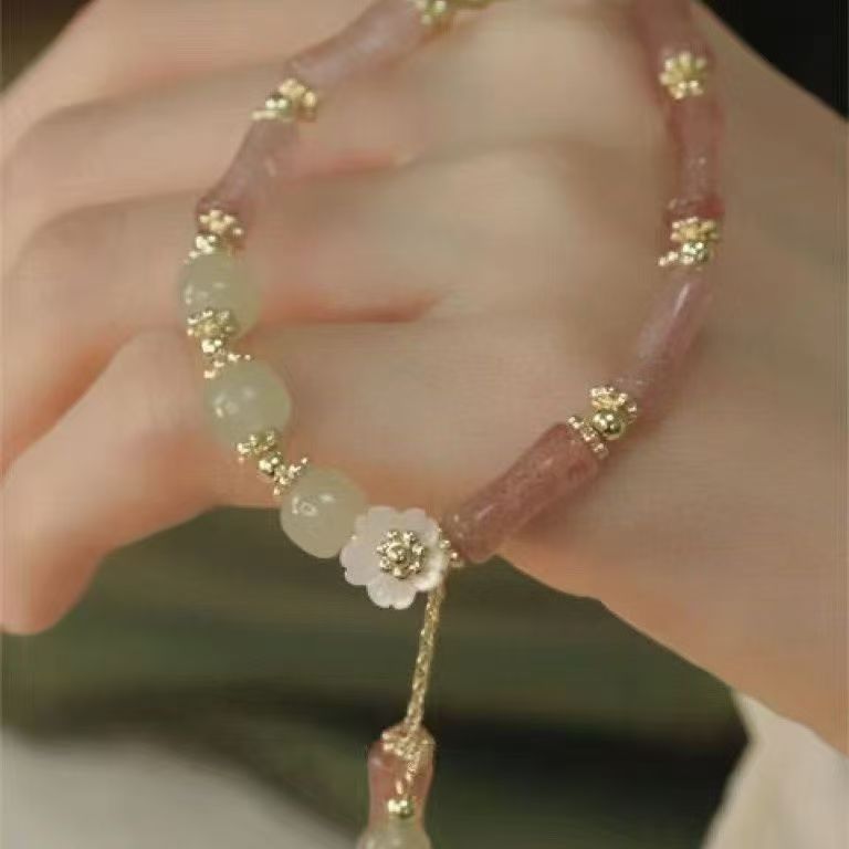 Close up of a pink crystal beaded bracelet with a white flower charm on a wrist