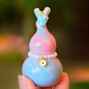 A small pastel blue and pink painted wooden gourd charm held between fingers