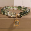 Close-up of a Green Phantom crystal bracelet with a gold wire-wrapped pendant on a box.