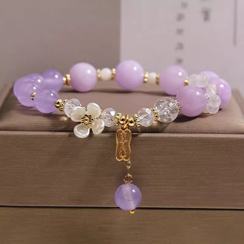 Close up of lavender amethyst beaded bracelet with white flower beads and gold charm