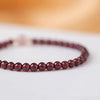 Close up of a red garnet beaded bracelet with a pink stone worn on a wrist