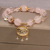 Pink crystal beaded bracelet with a gold-tone longevity lock charm on a beige box