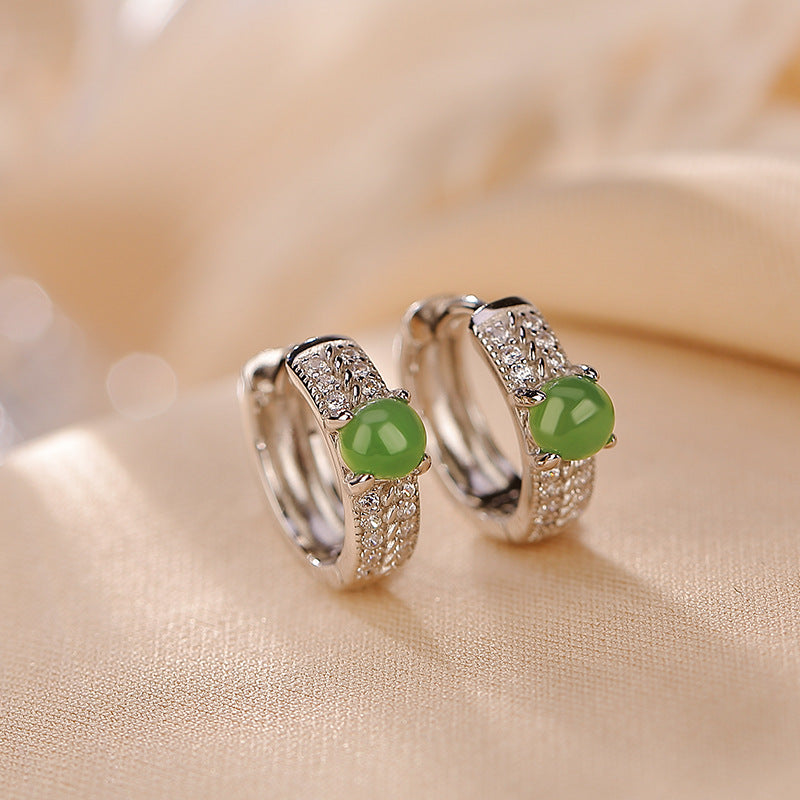 Pair of sterling silver hoop earrings with green jade beads on beige fabric