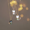 Three variations of a gold tone cat pendant necklace with pearl or jade accents against a bokeh background