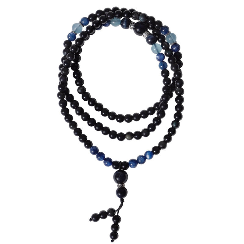A coiled strand of black obsidian and blue kyanite beads resting on a wooden jewelry tray.