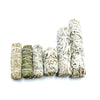 Several sizes of dried white sage smudge sticks lined up on a white background