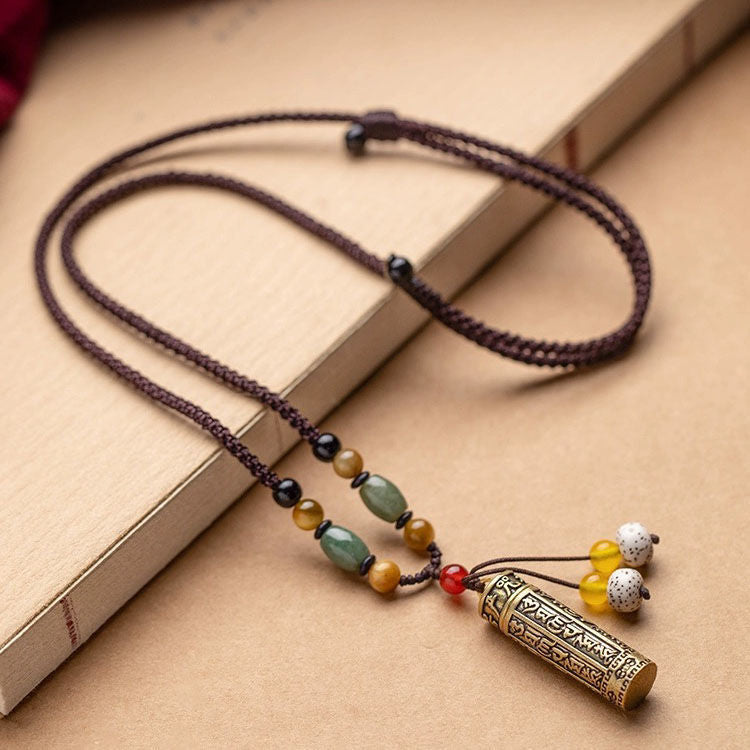 Gold-tone cylindrical pendant with engraved mantras on a braided brown cord