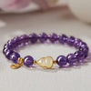 Close up of a purple beaded bracelet with a gold gourd charm on a white surface